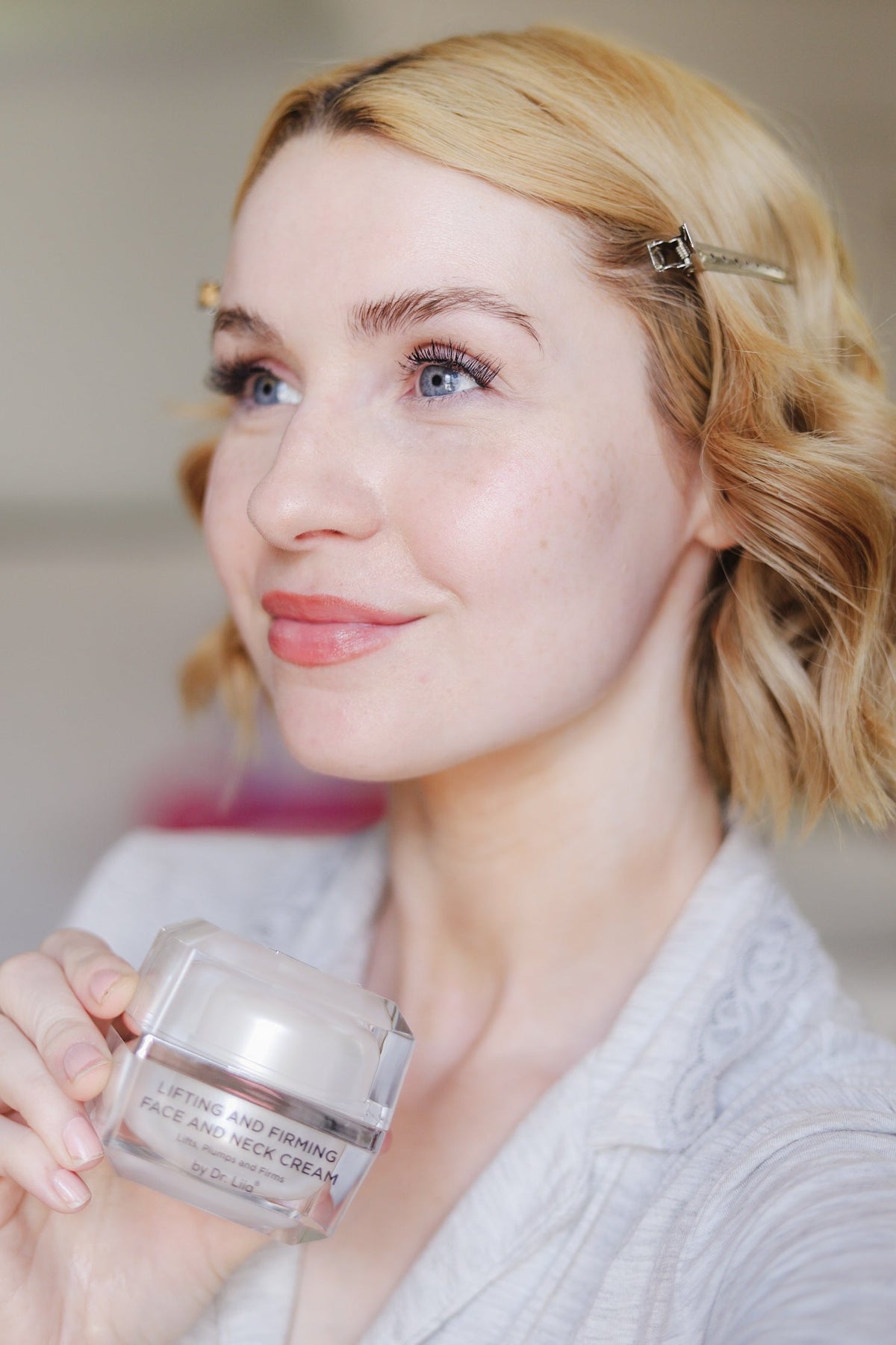 Woman with wavy blonde hair holding the cream jar near her chest