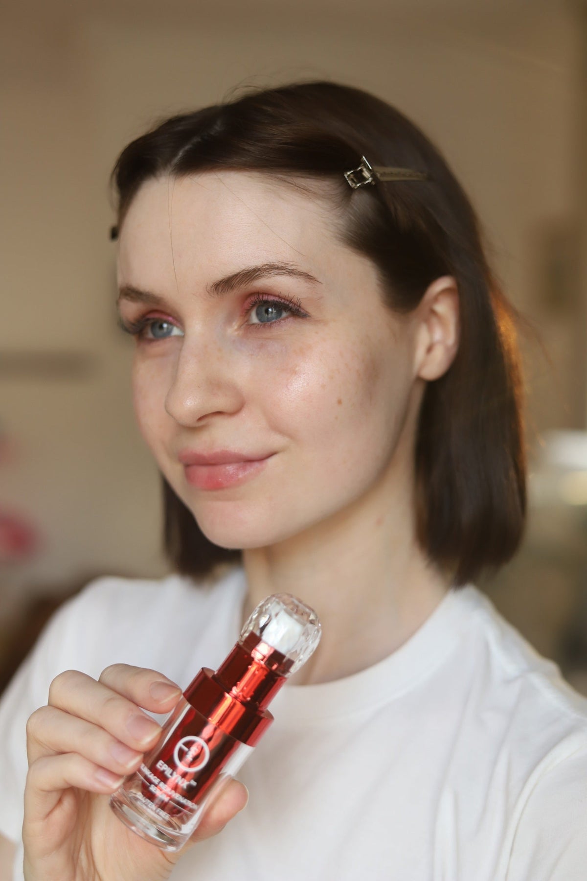 Woman in a white T-shirt holding the red serum bottle near her shoulder