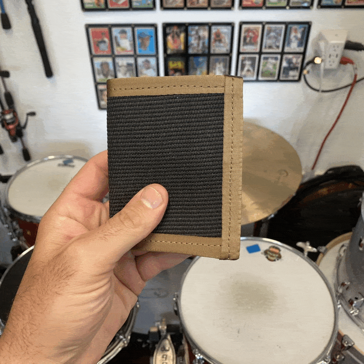 Hand holding the open tan wallet in front of a drum kit, showing card slots and an ID window