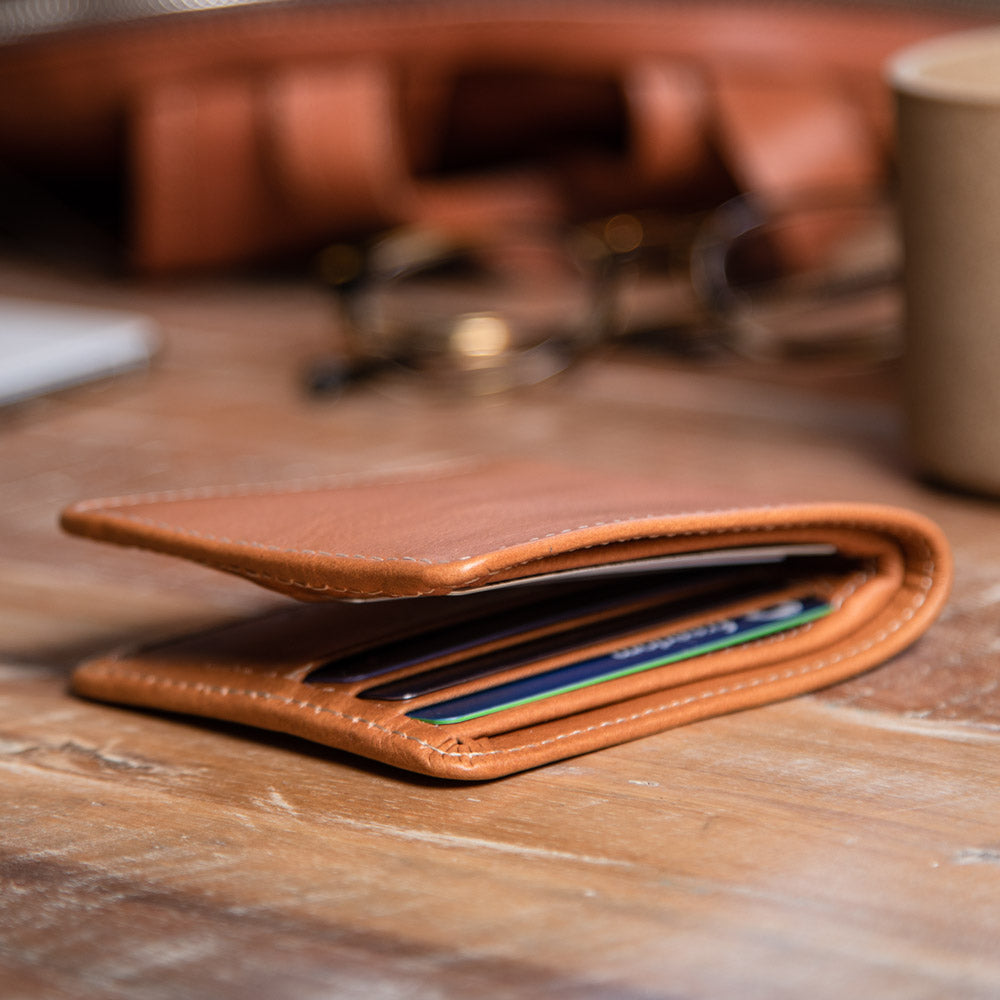 Tan leather billfold lying open on a wooden surface with cards in its slots