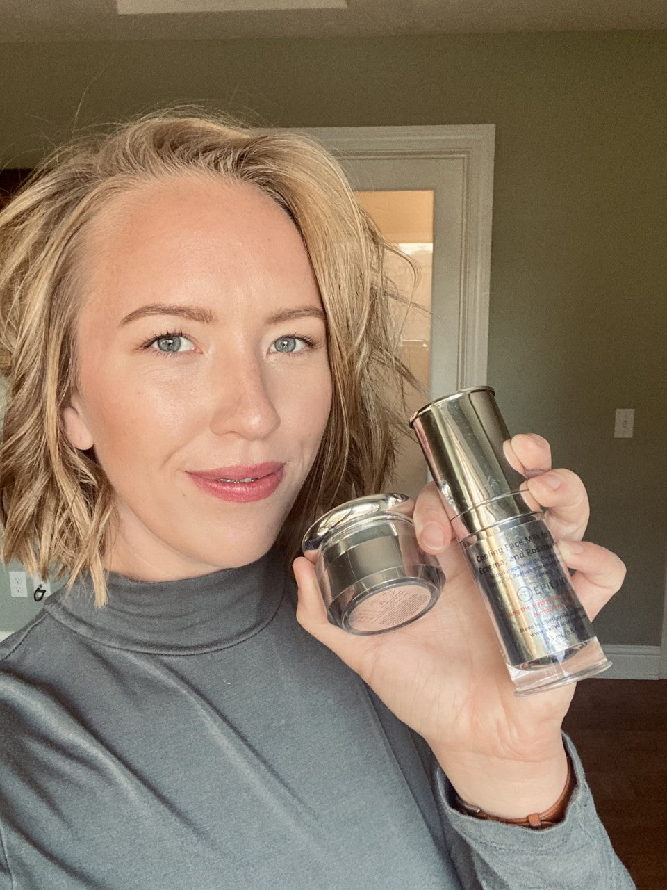 Woman in a gray top holding the EpiLynx moisturizer bottle and its cap near her face