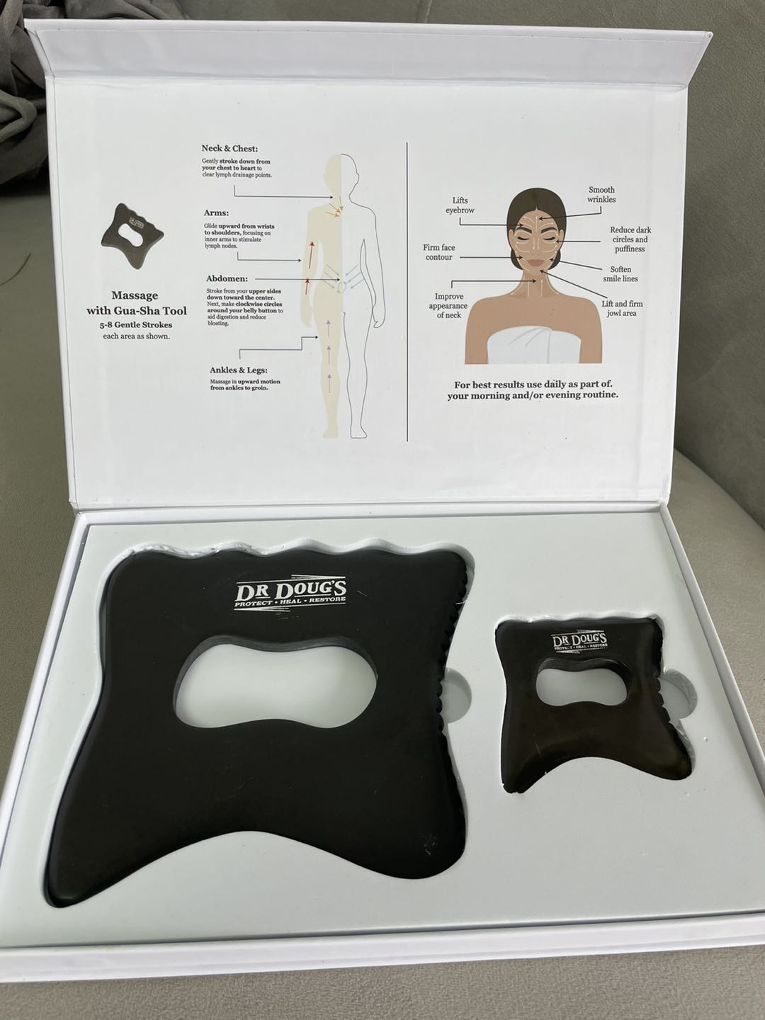 Large and small black gua sha tools in an open white gift box with an instruction card