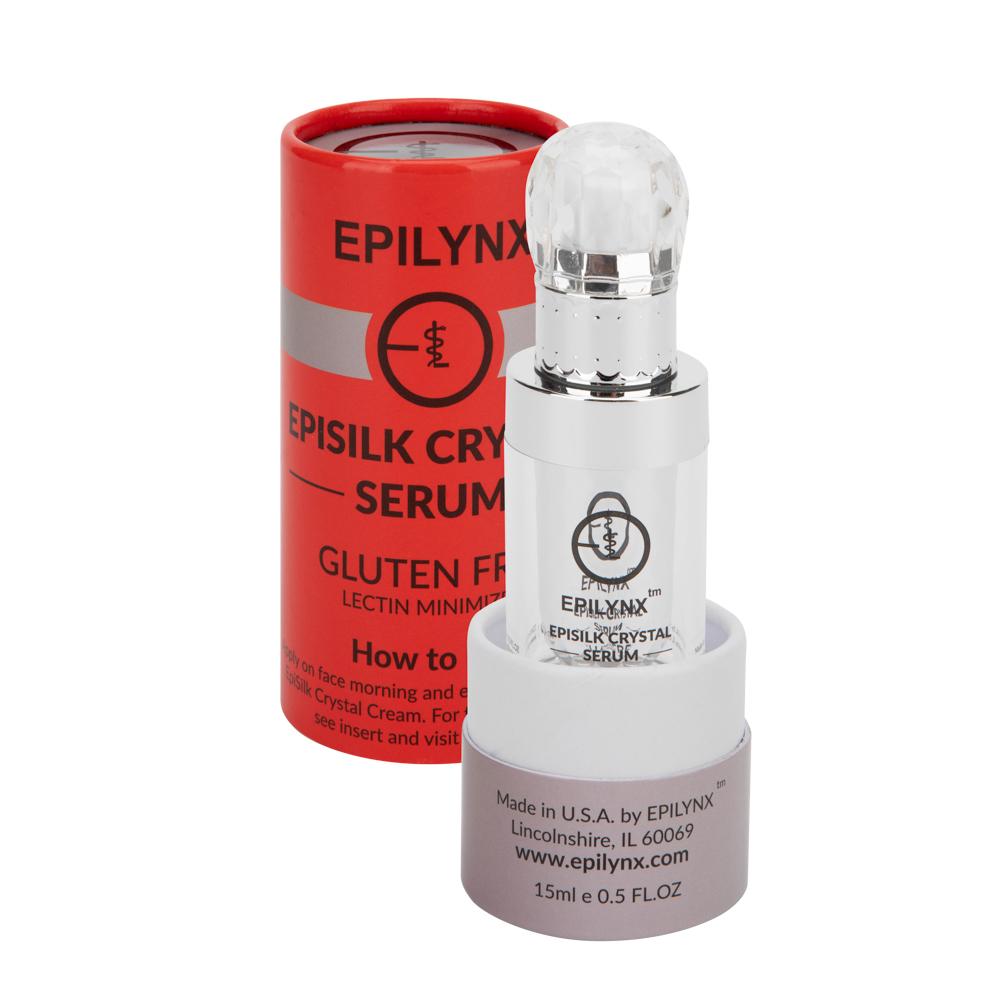 Silver serum bottle in front of its red cylindrical box and a small jar